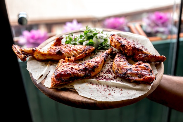 Free photo front view a man holds a tray with grilled chicken thighs on a pita with onions and herbs