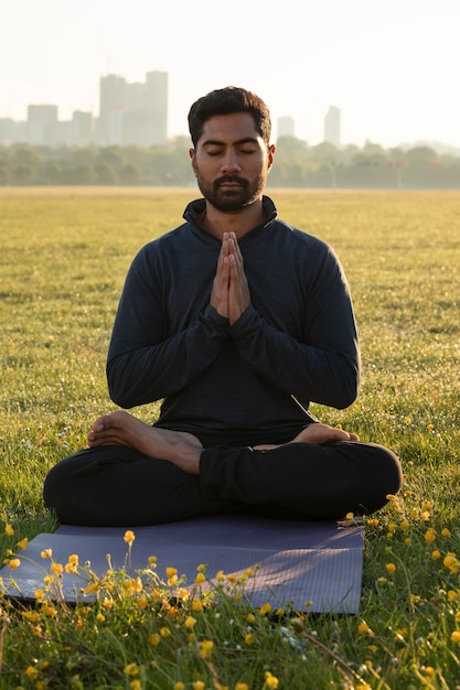 Front view of man meditating outdoors on yoga mat