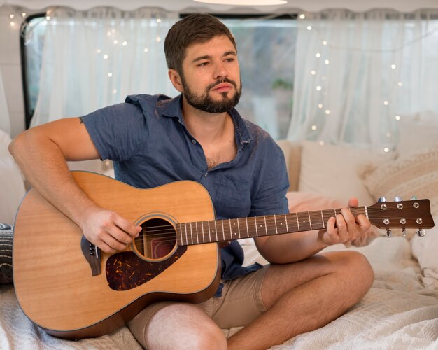 Front view man playing the guitar in a caravan