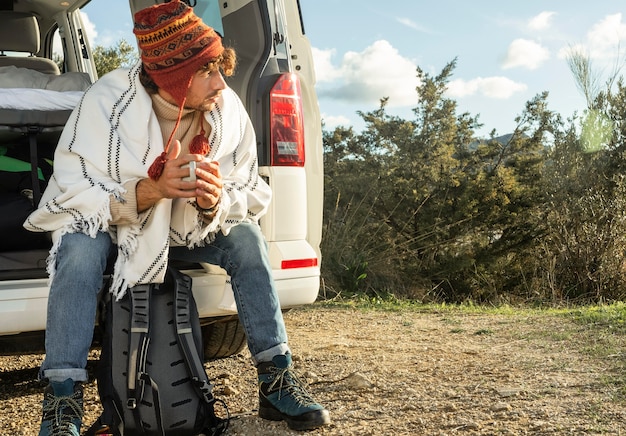 Front view of man sitting on the  trunk of the car while on a road trip