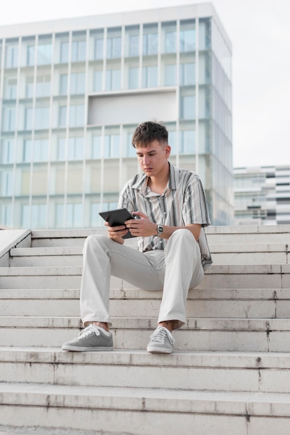 Front view of man on steps outdoors looking at tablet