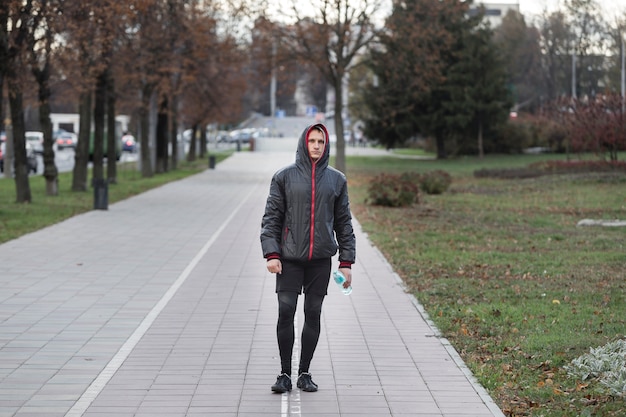 Front view man walking and holding a bottle of water