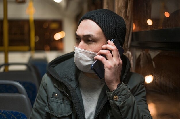 Front view of man wearing medical mask in the bus and talking on the phone