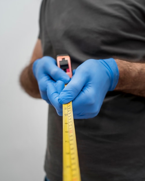 Free Photo front view of man with gloves holding tape measurer for social distancing