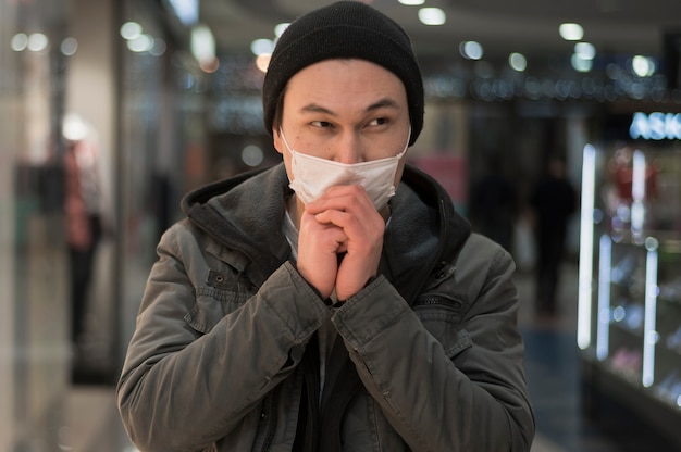 Front view of man with medical mask praying at the mall