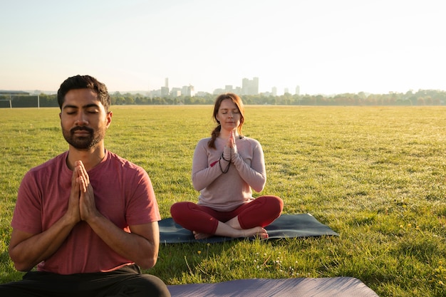 Free photo front view of man and woman meditating outdoors on yoga mats