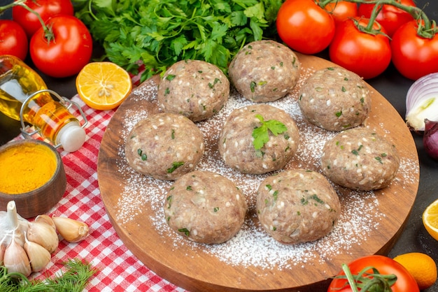 Free Photo front view of meat balls on a brown board and rice flour fresh green lemon fallen oil bottle fresh vegetables yellow ginger on red stripped towel on black background