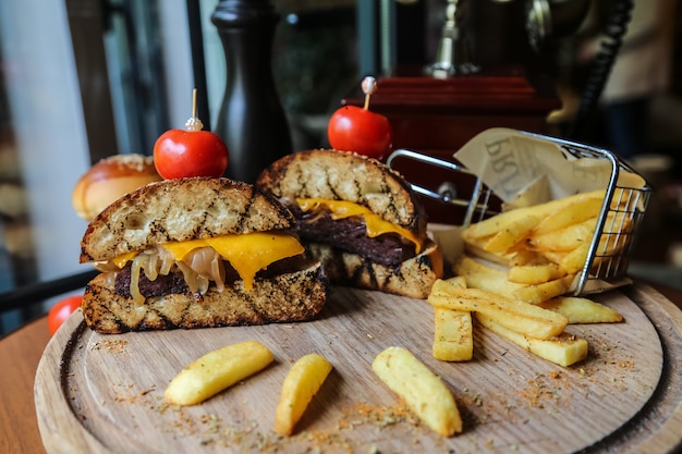 Front view meat burger halves with tomatoes and fries with spices on a stand