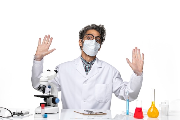 Free photo front view middle-aged scientist in special suit sitting around table with solutions