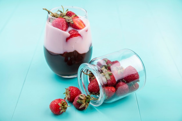 Free photo front view of milkshake with strawberries and chocolate on a glass on blue surface