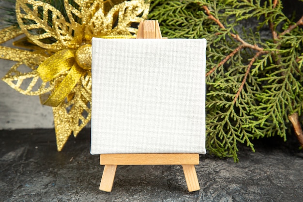 Free photo front view mini canvas on wooden easel pine branch xmas ornament on grey