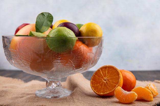 Free photo front view mix of fruits lemons  limes  plums  peaches and oranges in a vase on a beige napkin