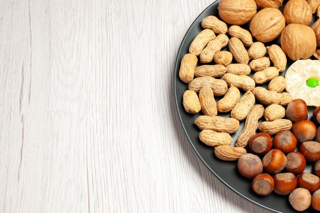 Front view nuts composition fresh walnuts peanuts and hazelnuts inside plate on the white desk nut tree snack plant many shell