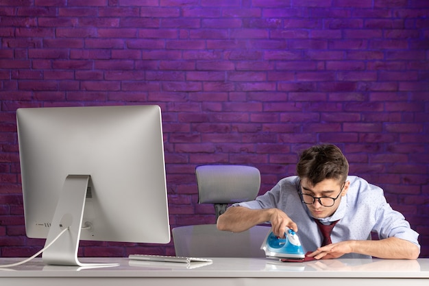 Free photo front view office worker behind office desk ironing his tie