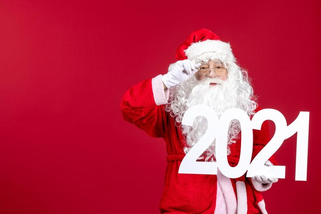 Front view of old santa claus holding writing on red wall