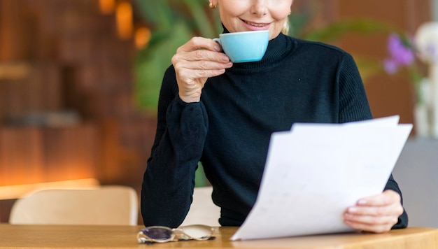 Front view of older business woman reading papers while having coffee