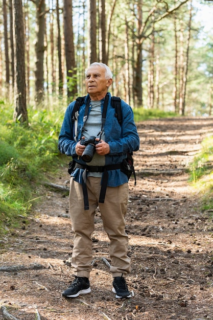 Front view of older man traveling with backpack and camera in nature