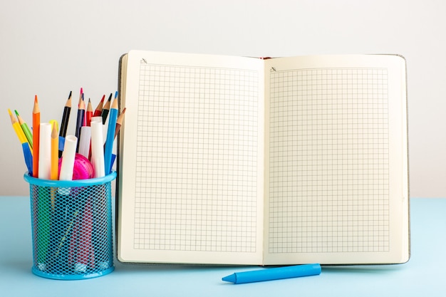 Free Photo front view open copybook with felt pens and pencils on blue desk