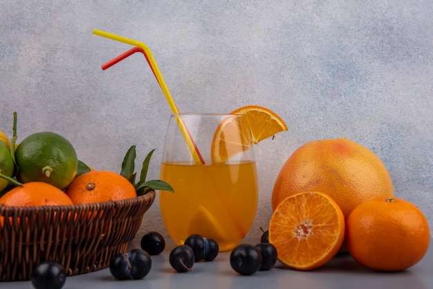 Free photo front view oranges with lemons and limes in a basket with orange juice in a glass with strawberries on a gray background