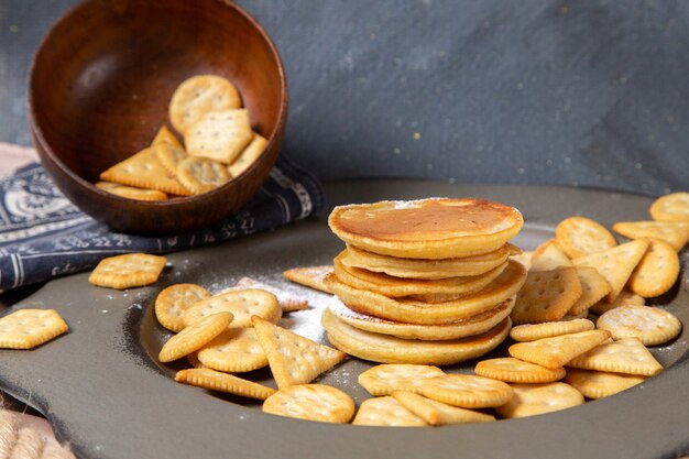 Front view pancakes and crackers inside plate on grey