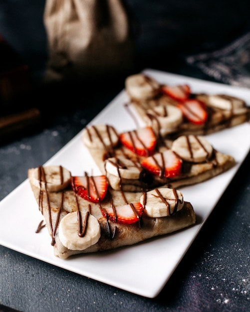 Free Photo front view pancakes sliced with strawberries and bananas inside white plate on the grey desk