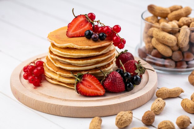 Front view pancakes with strawberries black and red currants on a tray with peanuts