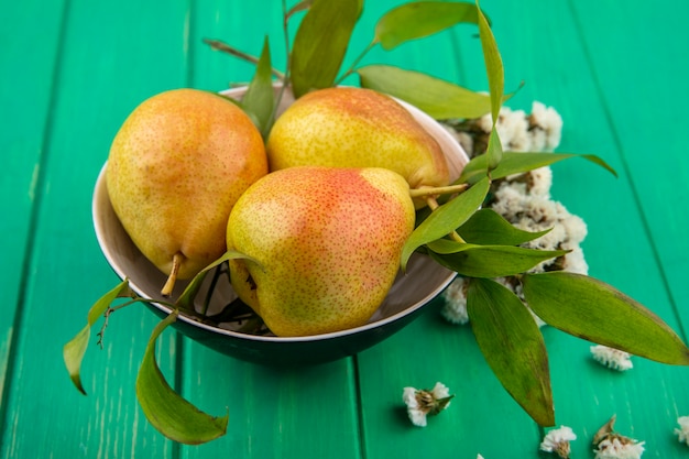 Front view of peaches in bowl with flowers on green surface