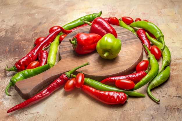 Front view peppers on a chopping board surrounded by peppers and cherry tomatoes on amber background