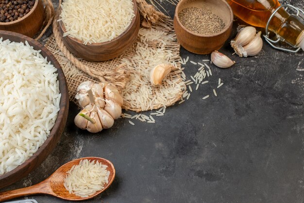 Front view of perfect long rice brown bowls on nude color towel fallen oil bottle garlics peppers on dark table