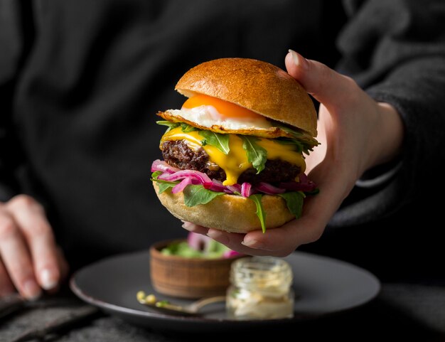 Front view person holding burger with fried egg