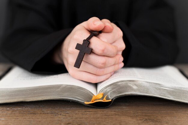 Front view of person praying with cross and holy book