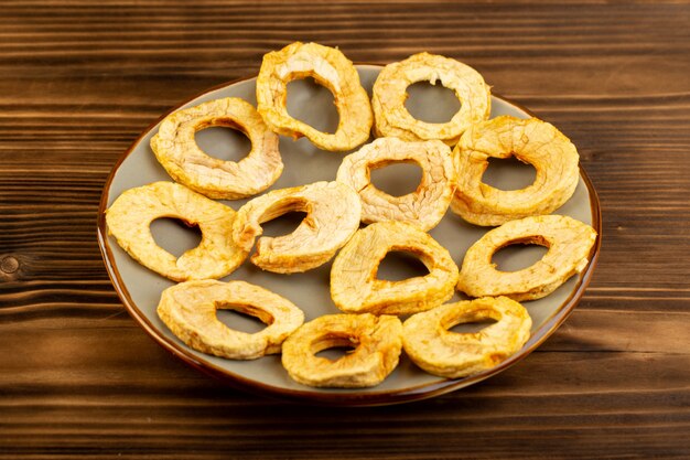 A front view pineapple dried rings inside plate dried fruits sour tasty unique taste on the brown wooden desk fruits exotic dry