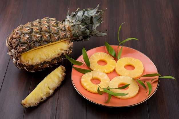 Front view of pineapple with one piece cut out from whole fruit with pineapple slices in plate on wooden surface