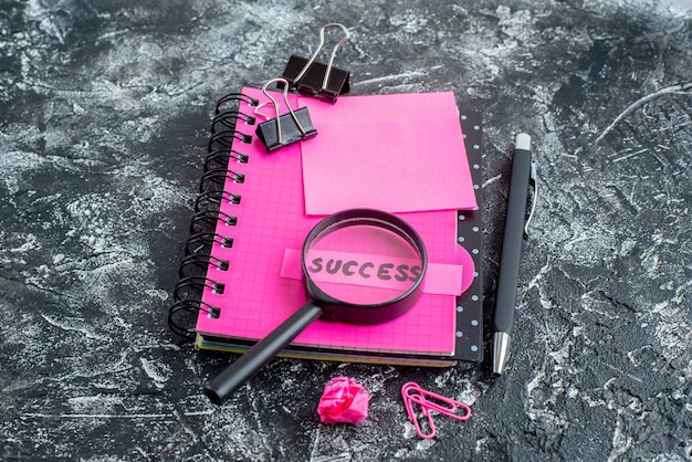 front view pink notepad with pen magnifier and success note on gray background