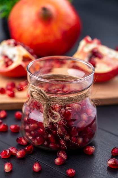 Free photo front view of pomegranate berries in glass jar with whole and cut one on cutting board on black surface