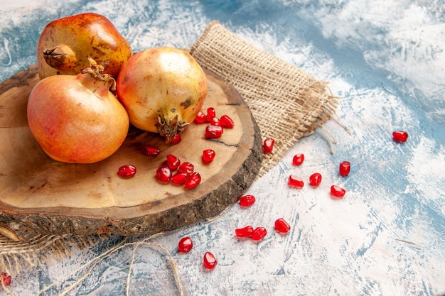 Free Photo front view pomegranates on round cutting board scattered pomegranate seeds on blue-white background free space