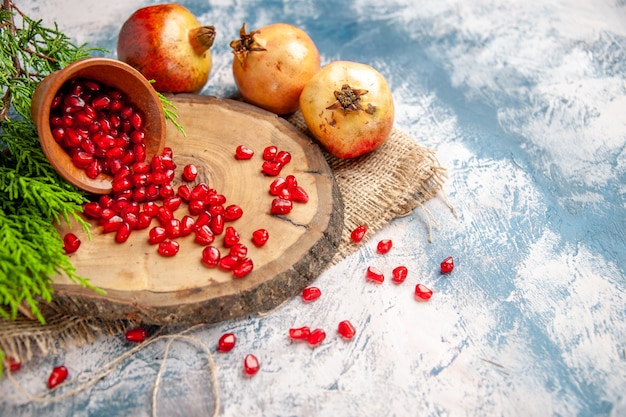 Free Photo front view pomegranates scattered pomegranate seeds in wooden bowl on round cutting board on blue-white background free place