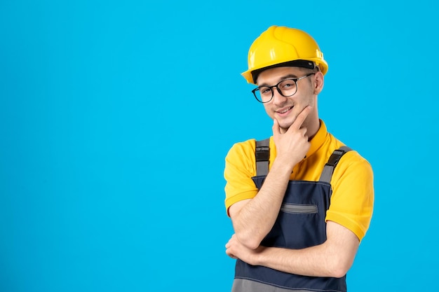 Front view of posing male builder in uniform and helmet on blue 