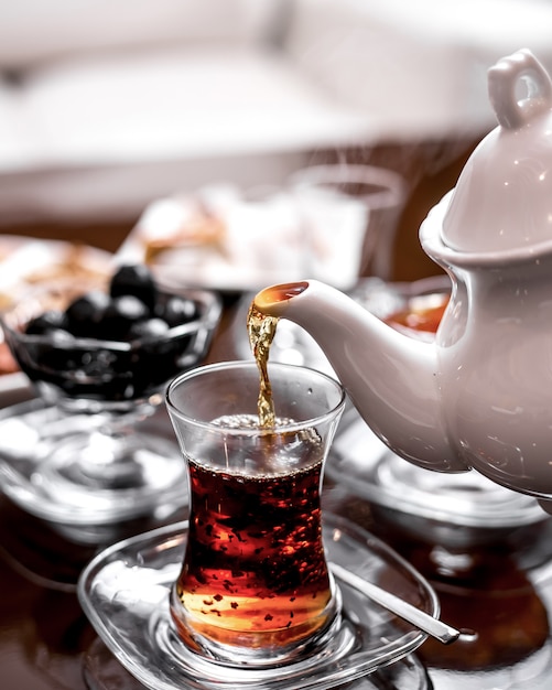 Front view pours tea into a glass of armudu from a tea kettle