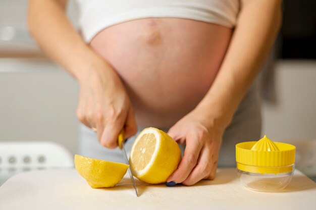 Front view pregnant woman hands cutting a lemon