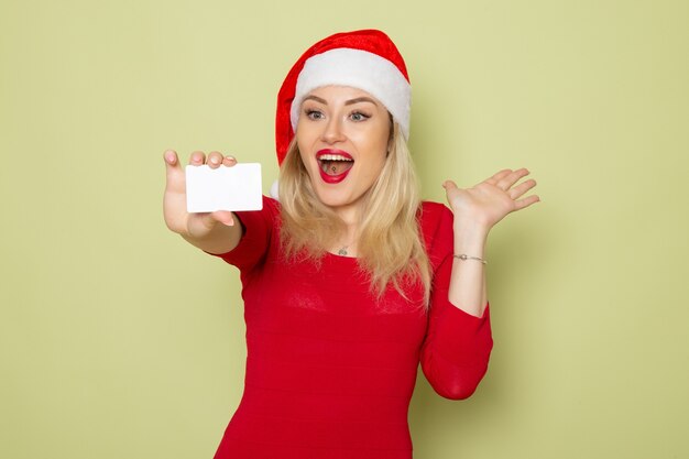 Front view pretty female holding bank card on green wall color christmas snow new year holiday emotions