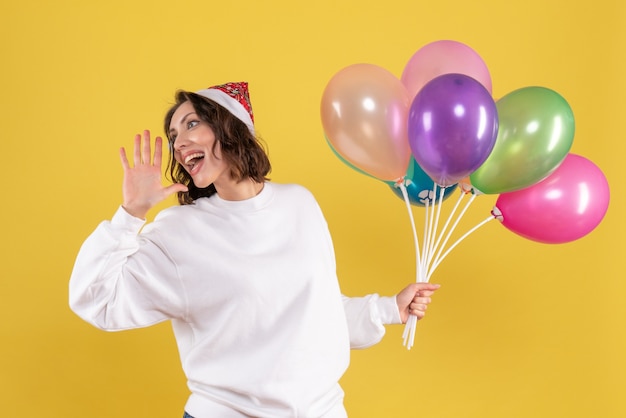 Front view pretty female holding colorful balloons on the yellow 