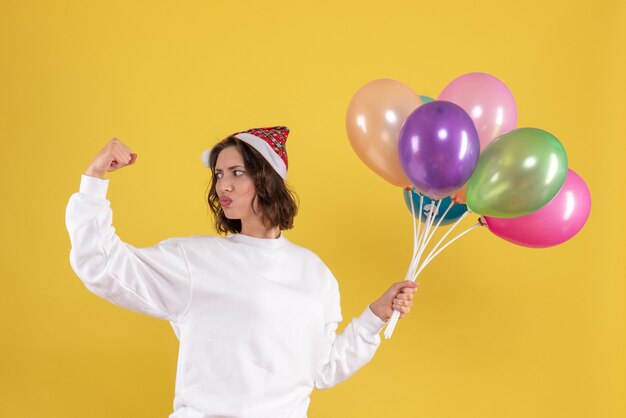 Front view pretty female holding colorful balloons on yellow 