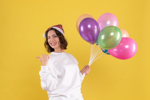 Front view pretty female holding colorful balloons on yellow 