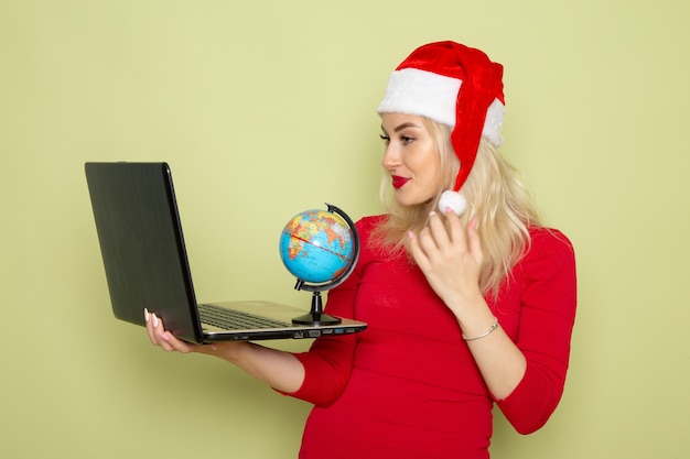 Free photo front view pretty female holding little earth globe and laptop on green wall christmas color snow holiday new year emotions