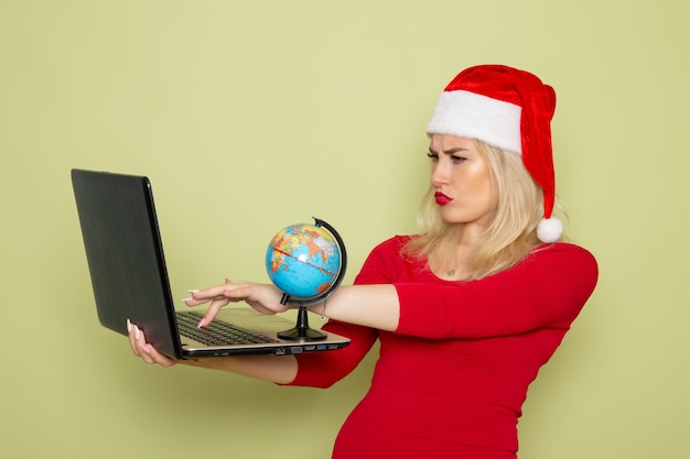 Free Photo front view pretty female holding little earth globe and laptop on green wall christmas snow holiday new year emotion