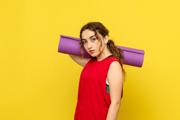 Front view of pretty female holding purple carpet on yellow