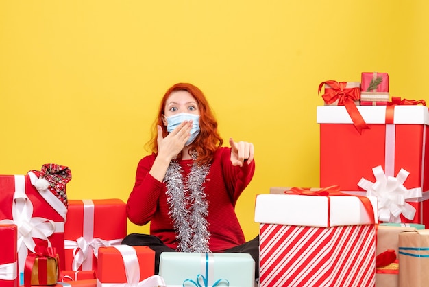 Front view pretty female sitting around presents in mask on yellow 