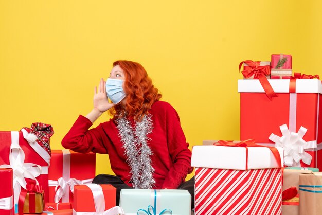 Front view pretty female sitting around presents in mask on yellow 