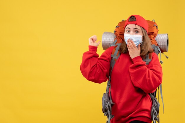 Front view puzzled female tourist with backpack and mask pointing at behind